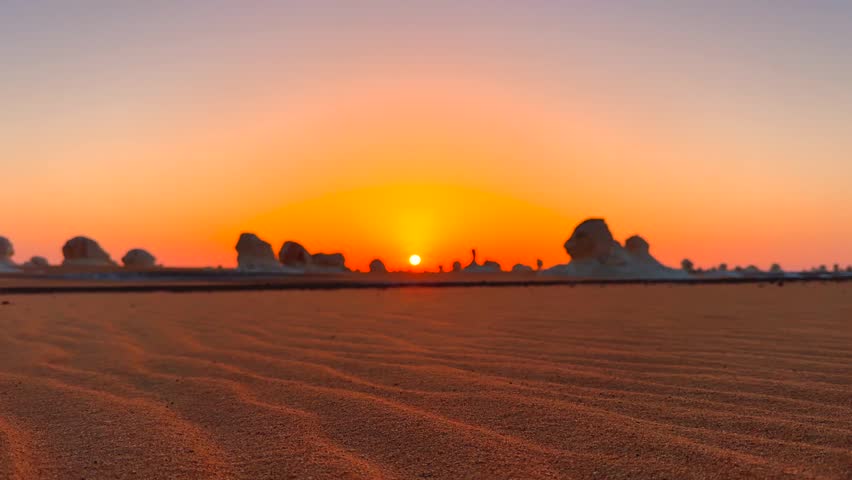 Golden sunrise illuminating surreal rock silhouettes in desert landscape of White Desert, Egypt