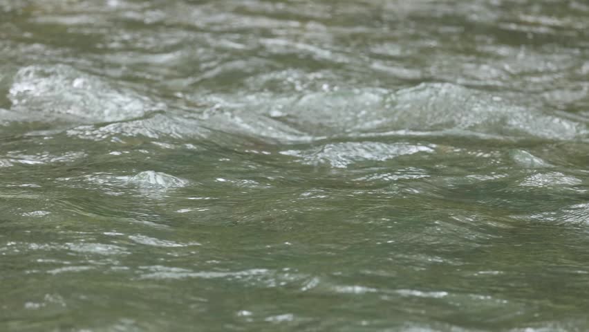 Rapid water flow creates ripples, a dynamic natural liquid motion background.