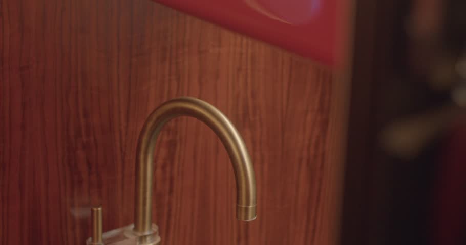 Detailed image of brass faucet on contemporary marble countertop. Closeup photograph displaying brass faucet mounted on modern marble surface with warm wooden accents
