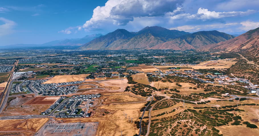 Urban area of Spanish Fork, Utah, USA scattered in the vast valley. Fluffy clouds hang over the gorgeous mountains. Aerial view.