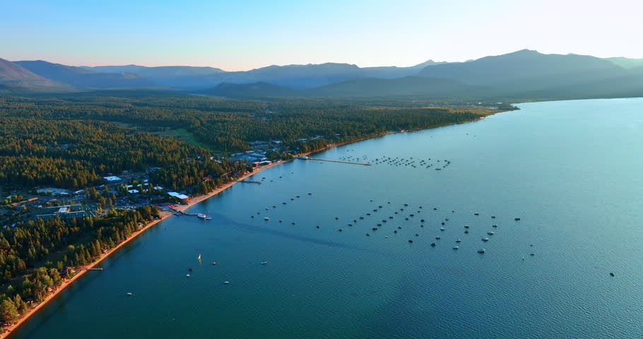 Approaching yachts and boats standing on the peaceful waterscape of Lake Tahoe, California, USA. Pine tree woods and spectacular mountains at backdrop. Aerial view.