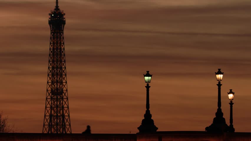 Silhouette of tower and street lights during sunset with orange sky.