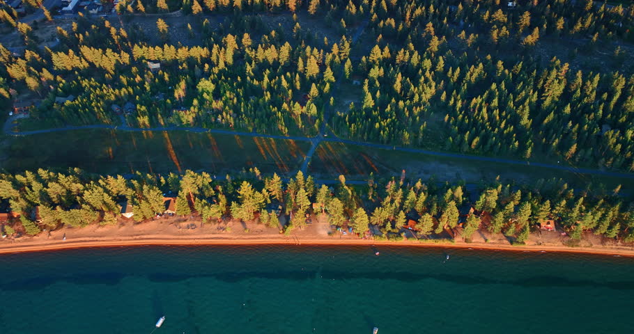 Footage over the lakefront with narrow sandy beach and pine tree woods. View on the nature and infrastructure of Lake Tahoe, California, USA.