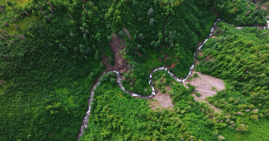 Wavy narrow river flowing by the mountainous area. Drone flight over the rocky landscape in the wilderness of Alaska, USA.