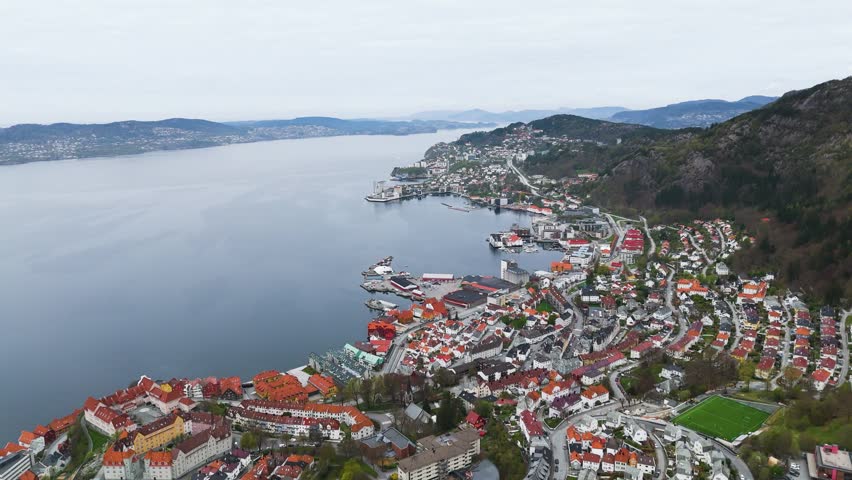 residential buildings follow curve shoreline seaside town green athletic field sits base tree covered mountain norway bergen city center port tree-covered urban landscape