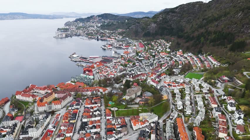 orange white roofs cascade calm fjord coastal town steep dark green mountain valley frame small sports field toward down norway bergen city center port lush water nature wilderness
