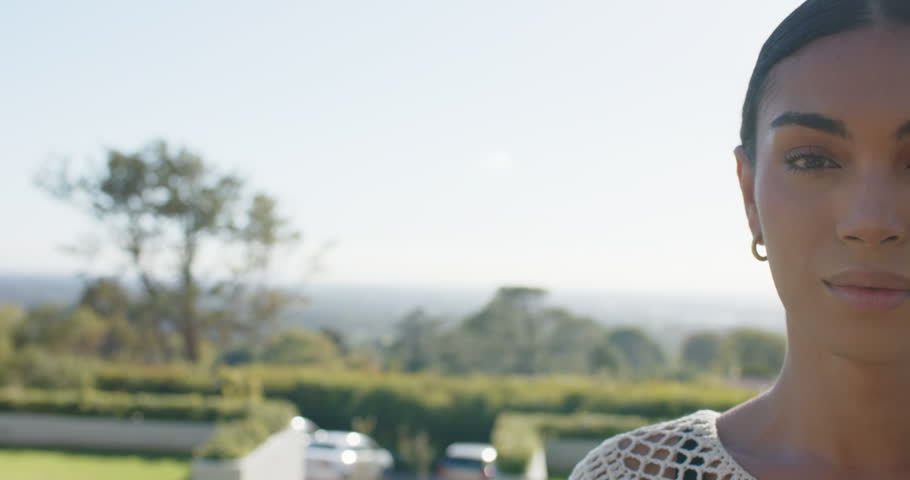 Cam revealing African American woman smiling, laughing on terrace in white crochet top, copy space. Balcony, female, outdoor, garden, hedges, driveway, landscape