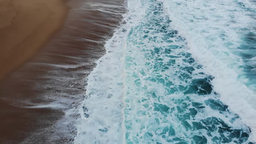 Ocean waves crashing on sandy beach creating beautiful patterns with foamy whitecaps motion footage.