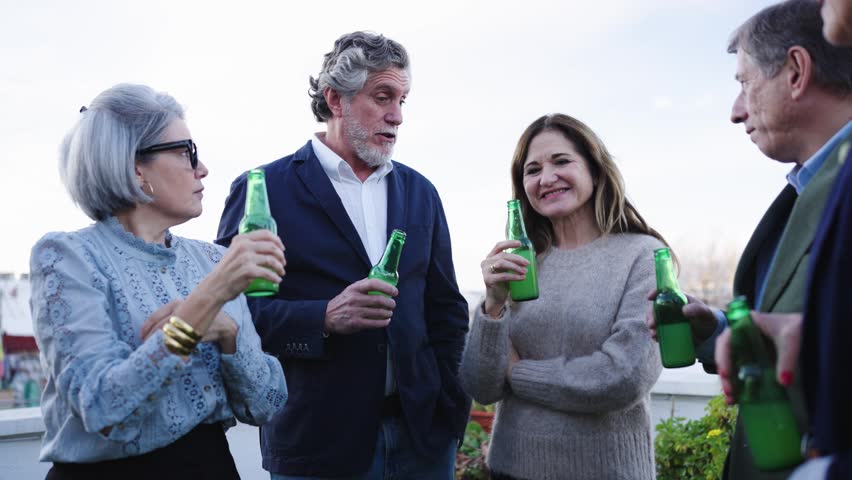 Mature men and women enjoying a conversation while drinking beer together. Happy senior friends socializing and having fun on a terrace party