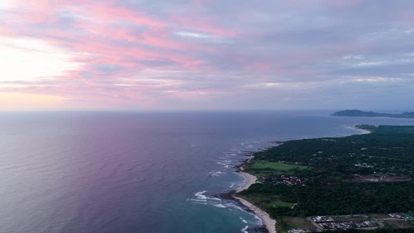 Stunning aerial perspective of the lush costa rican coastline at avellanas beach. The pacific ocean meets a sandy shore and dense forest under a sky painted with vibrant pink and purple sunset clouds