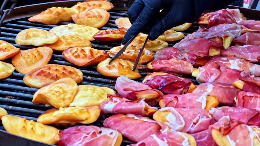 Chef grilling traditional polish oscypek cheese, some wrapped in bacon, at a street food stall in Krakow, Poland