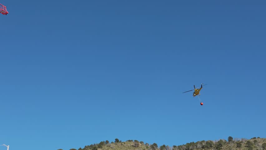 Firefighting helicopter with water bucket battling forest fire in Benidorm, Spain.