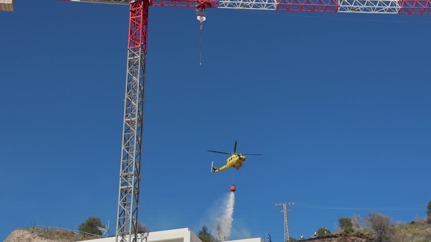 Firefighting helicopter dropping water on forest fire near residential area, Spain.