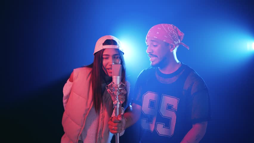 Energetic duo of singers, a man and a woman, performing a song together in a professional recording studio with vibrant blue stage lights