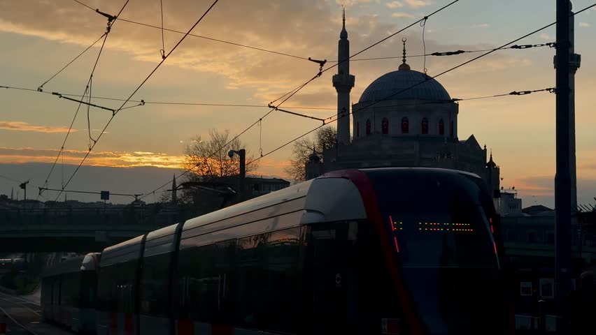A vibrant and scenic high-angle shot of a modern red tram traveling through the historic heart of Istanbul, Turkey. The tram moves along its tracks, surrounded by the city