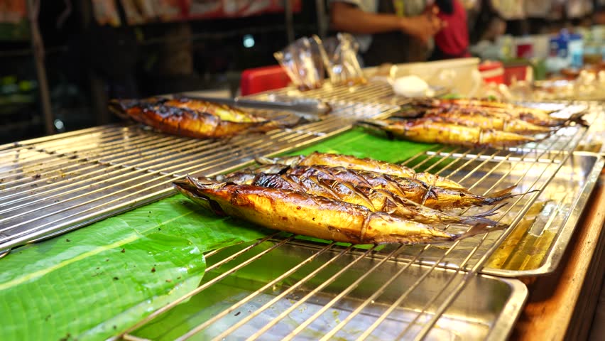 Street food market stalls with local fast food in Asia, various unhealthy junk food snacks on sale for locals and tourists, vendor sells exotic grilled seafood fish for customers on street in Thailand
