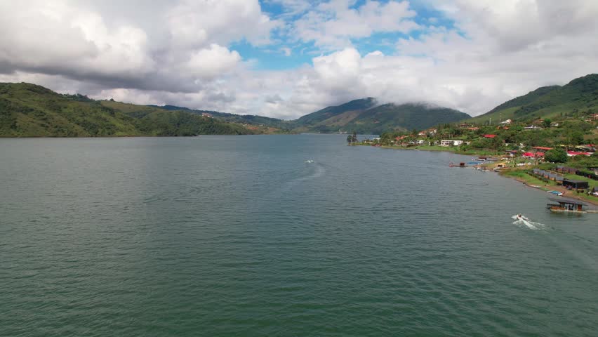 Aerial view of a beautiful lake surrounded by green mountains and a small village on a cloudy day