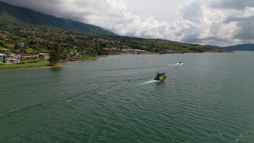 Aerial view of a colorful tour boat navigating across a tranquil lake near a mountainous shore