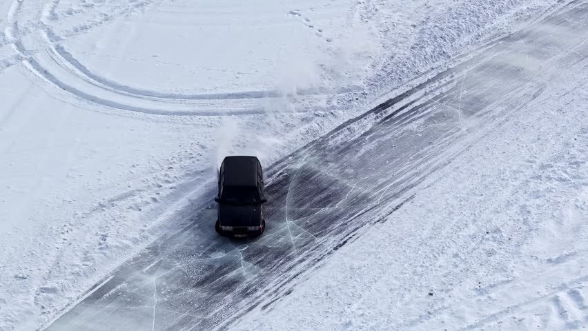 Aerial view of a car drifting on an icy winter track, sliding through a frozen curve with tire marks on snow for motorsport and driving skill content.