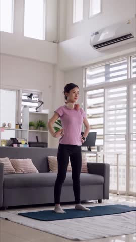 Young Asian woman stretching on yoga mat inside bright living room promotes healthy lifestyle fitness calm well being at home
