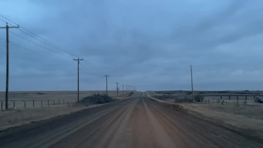 Quiet rural gravel road at dusk with open fields