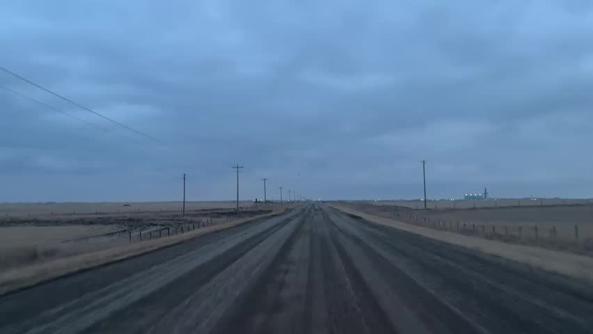 Rural gravel road through open prairie with dark clouds and empty landscape in Alberta