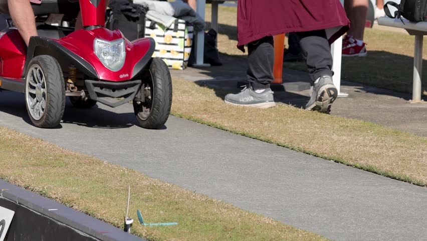 Mobility scooter, person, paved path, onlookers, outdoor motion.