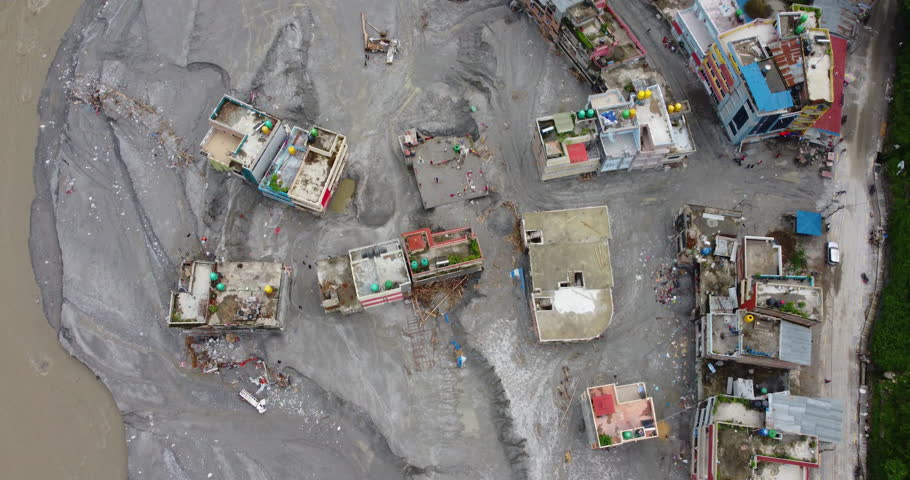 Top-down aerial shot capturing the destructive aftermath of the Melamchi Nepal river flood with vast layers of silt and debris covering a landscape of isolated homes, a vulnerable mountain community.