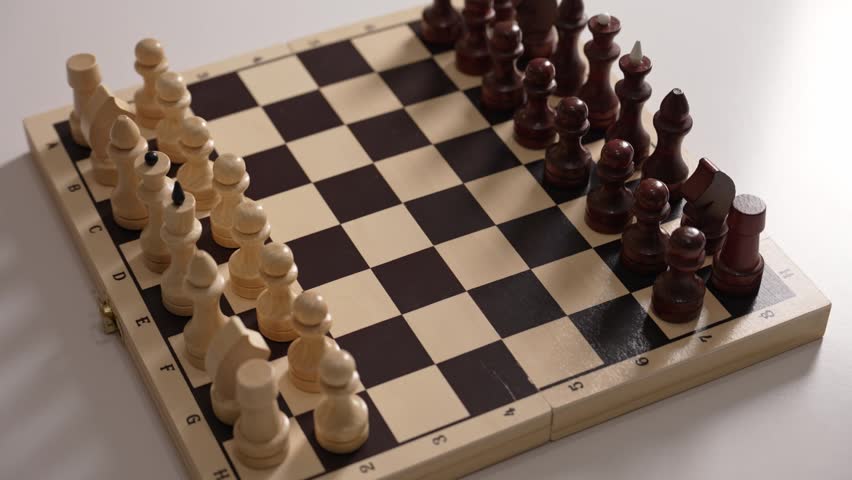 Player starting a chess match by moving a white pawn two squares forward, executing a strategic opening move on a classic wooden checkerboard against the black pieces on a white background