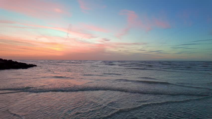 Serene ocean waves on a tranquil beach during a breathtaking pastel sunset. Cinematic footage of a colorful sky reflecting on the calm sea at dusk.