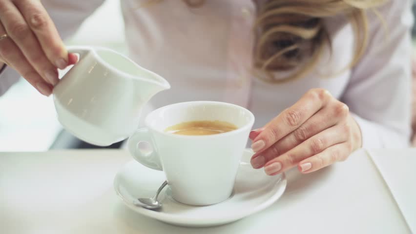 Woman adding cream to coffee cup, close-up shot, preparing morning beverage for enjoyment.