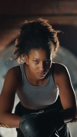 Portrait of young black woman resting after boxing workout in training center, sportswoman fastening boxing gloves. Slender female person do sport for stay healthy and slender, cardio workout