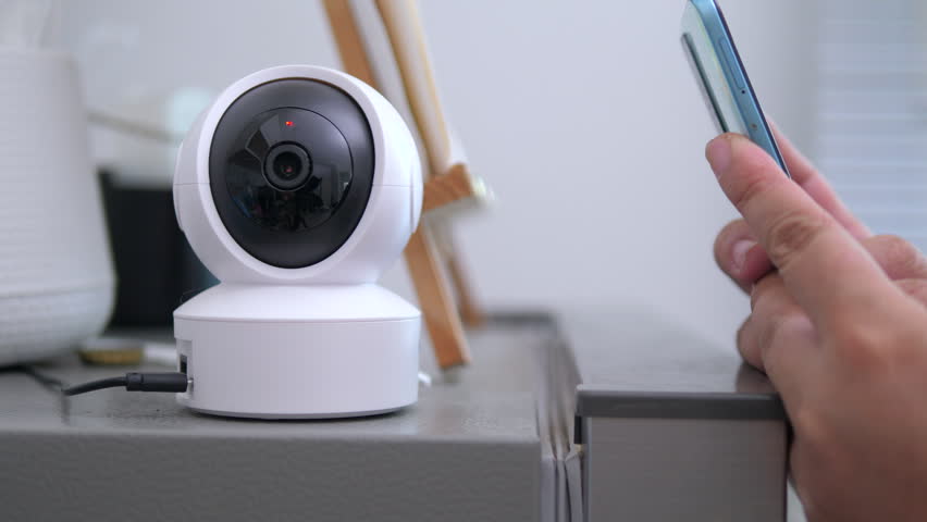 Person using smartphone to control IP camera for home security monitoring. Ideal for smart home technology, remote surveillance, and connected device concepts