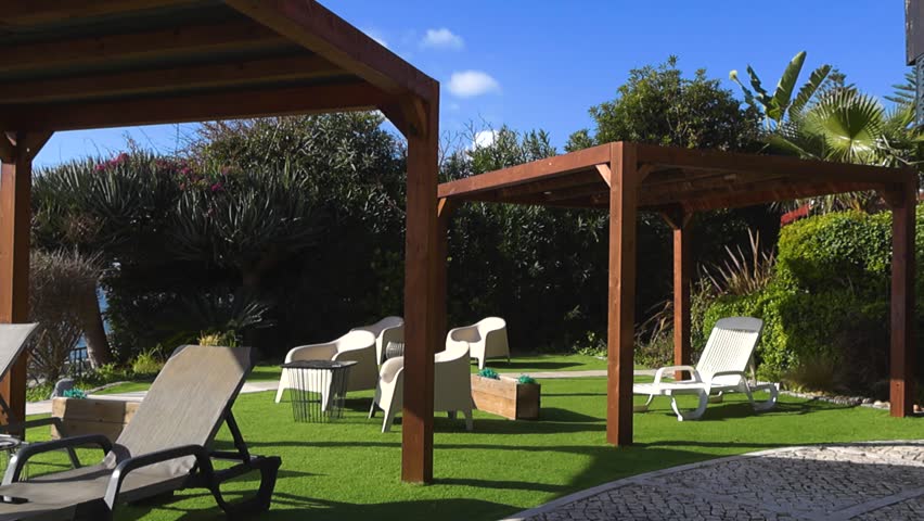 Beautiful outdoor lounge area at a luxury hotel with comfortable sunbeds and wooden pergolas on a lush green lawn overlooking the serene Atlantic Ocean on a sunny day in Portugal