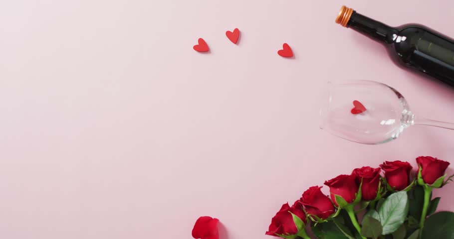 Red roses and wine glass with bottle on pink background at valentine