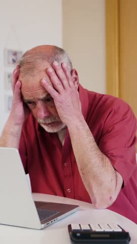 Elderly worried man sitting at a desk with a laptop and calculator, feeling stressed about finances, debt, and insurance expenses at home