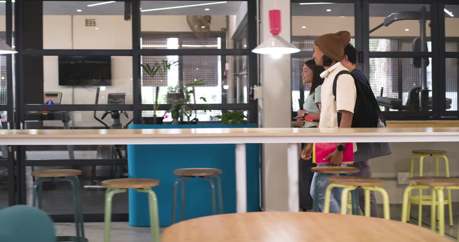 Diverse students walking into lounge, stopping, discussing notebooks for class while carrying bags. Trio, collaboration, study, coworking, campus, folders, backpack
