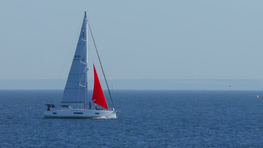 Sailing yacht moving across open water with red sail up.