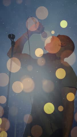 Vertical video: Singer giving intense vocal into wired mic, sparking bokeh overlay for live music. Vocalist, performer, microphone, stage, lighting, haze, vertical video