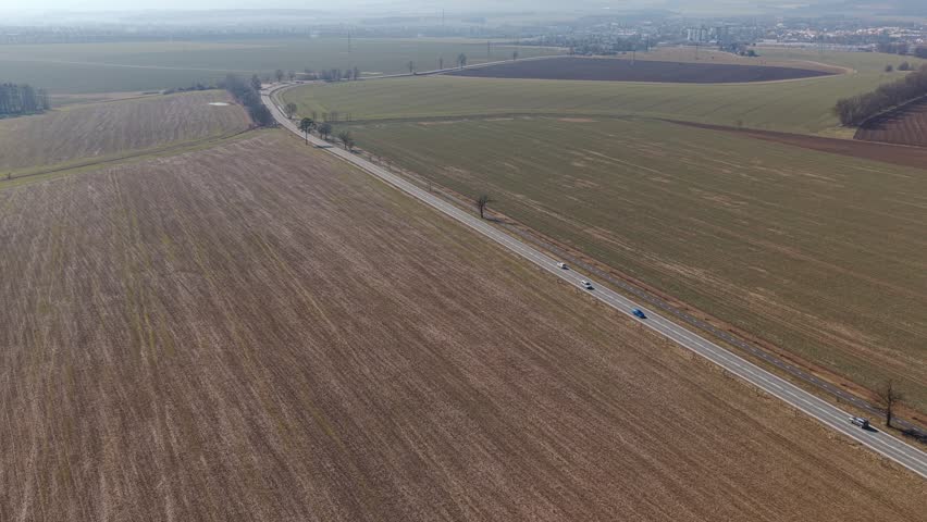 A road with passing cars and traffic in a rural landscape of fields. An aerial view on a sunny day