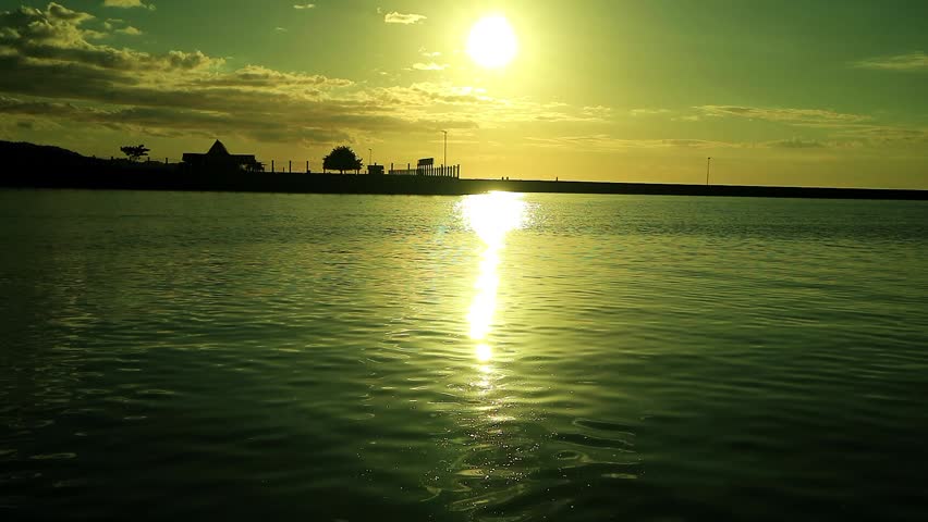 Beach view with calm water, pier and yellow sky at dusk in the background.
