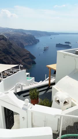 Panoramic view of Santorini island, Greece. Blue sea and the blue sky at sunny day. White architecture on the cliffs. Cruise ship near the coast. Vertical video
