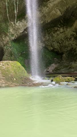 Waterfall flowing down rocky cliff into clear turquoise pool surrounded by green moss and forest
