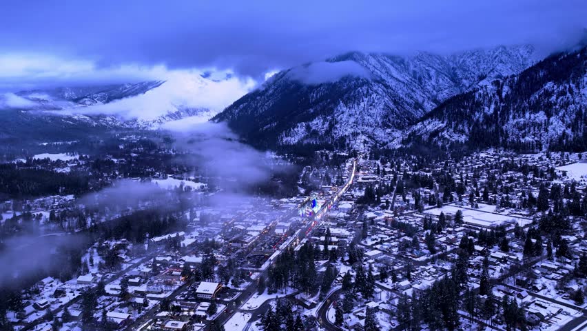 Snow-covered alpine town nestled among mountains, with fog rolling through the valley in a scenic winter landscape