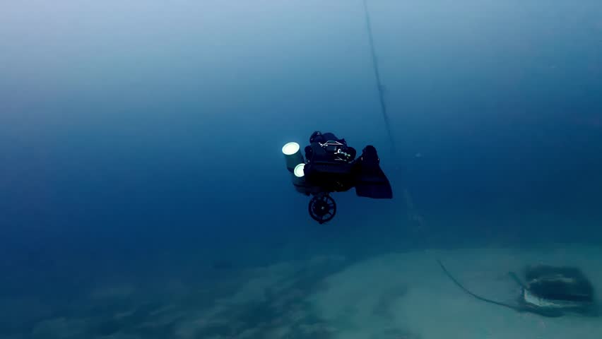 Deep blue underwater mystery of a technical diver exploring a shipwreck during autumn in the Mediterranean sea with clear visibility and dramatic low angle shot highlighting the vast aquatic abyss