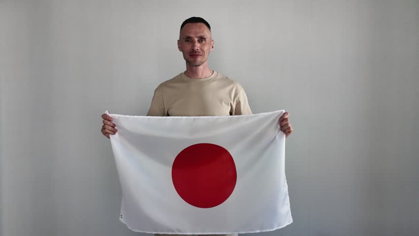 A happy man holds a Japanese flag. An enthusiastic fan cheers for his national team