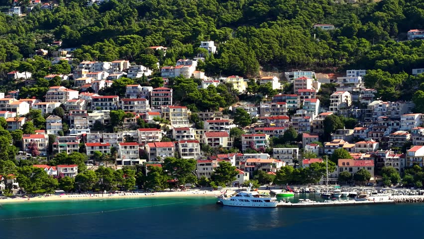 Scenic view of a coastal town in Croatia with red-roofed houses on a green hillside overlooking the Adriatic Sea and a harbor with boats