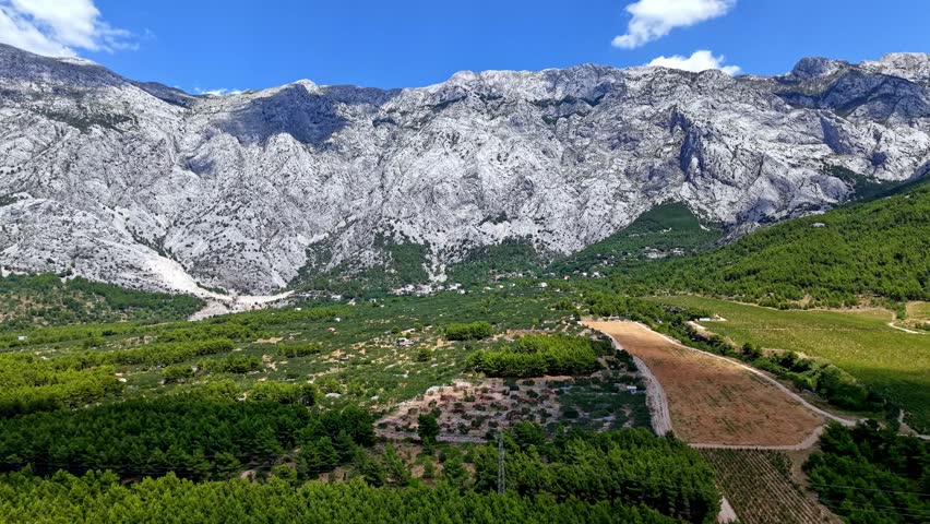 Scenic view of the Biokovo mountain range and green valley in Dalmatia, Croatia, under a blue sky