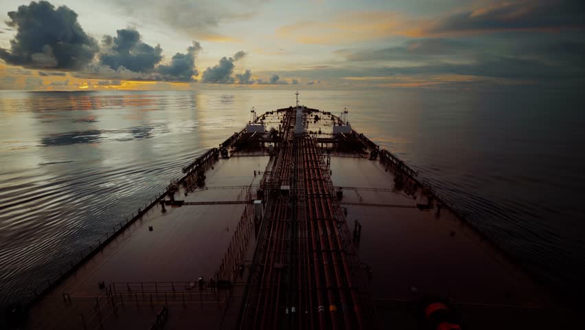 Oil tanker ship sailing on calm ocean waters at sunset, view from the bridge toward the bow