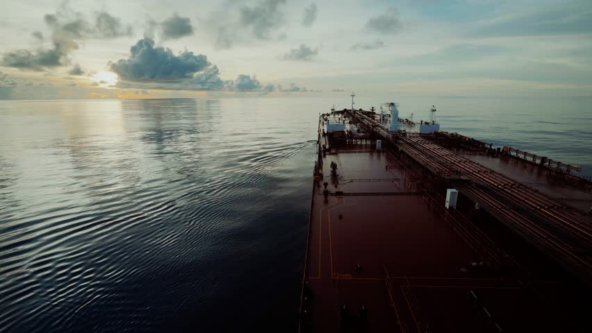 Oil tanker ship sailing on calm ocean waters at sunset, view from the bridge toward the bow